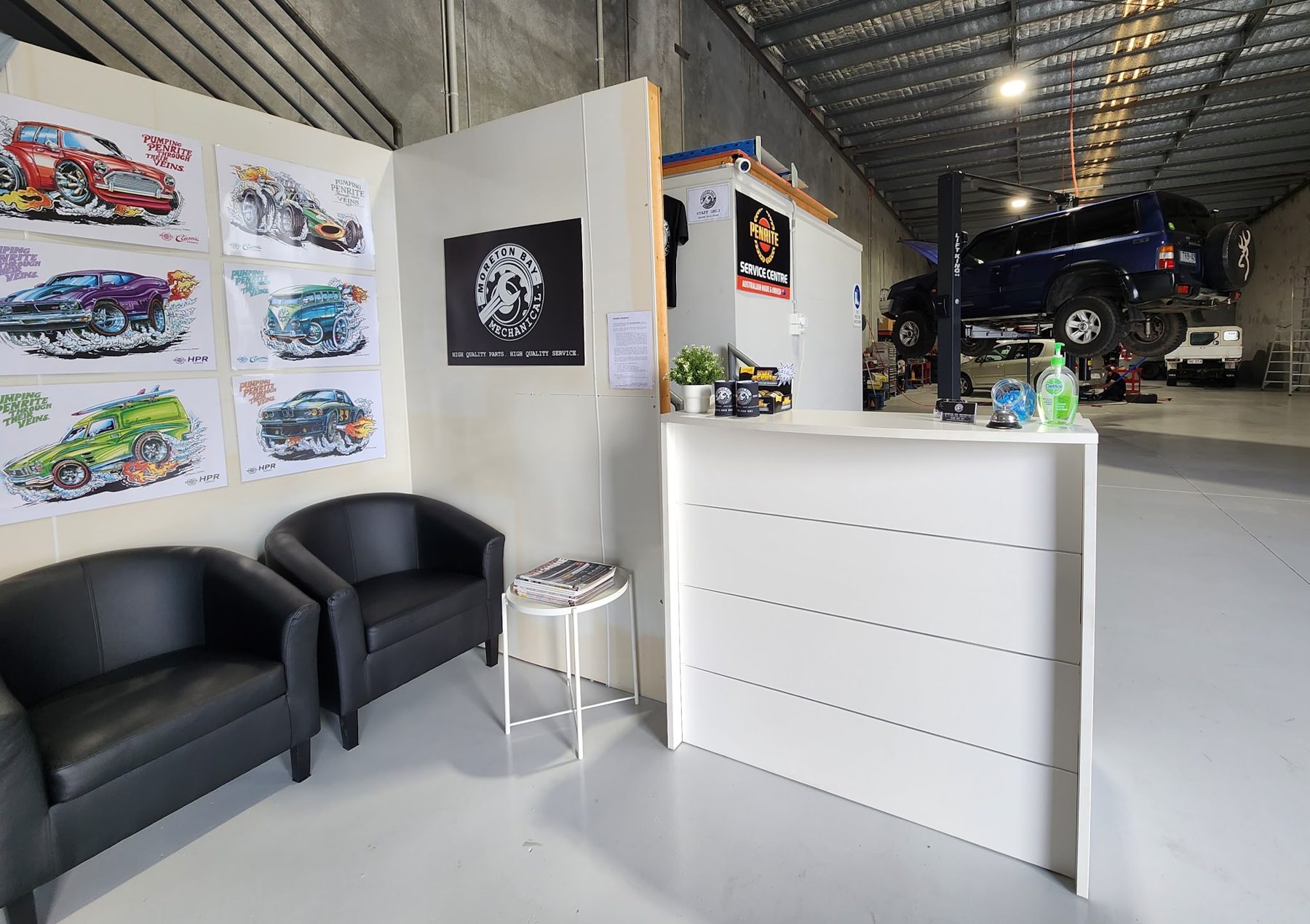 Reception and waiting area with leather chairs, the Moreton Bay Mechanical poster and a 4WD on the hoist behind