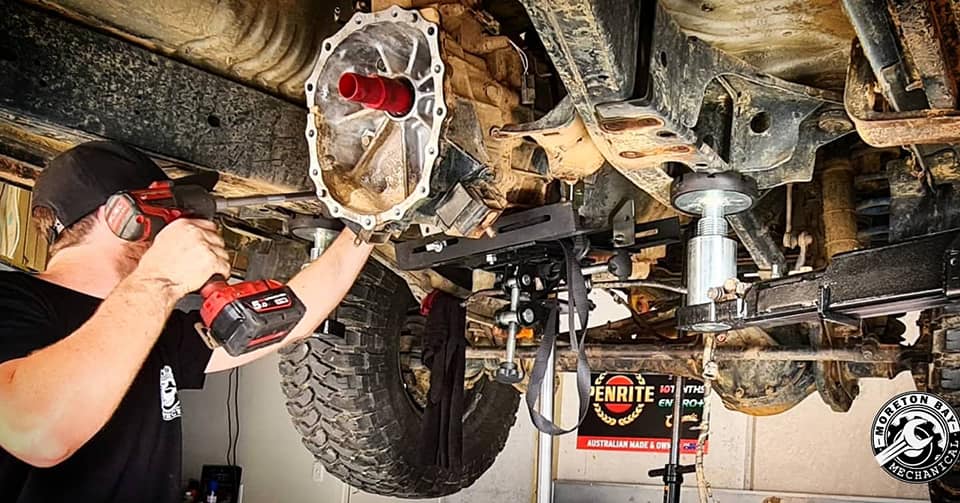Mechanic working on the underside of a 4WD on the hoist