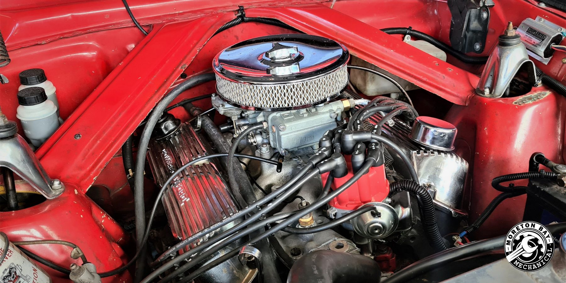 Chrome air cleaner and Holley carburettor in the red engine bay of a classic car